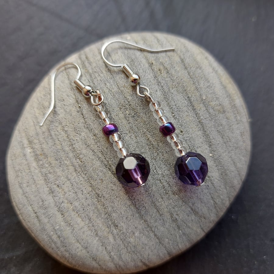 Drop earrings with faceted purple crystal and silvery seed beads.