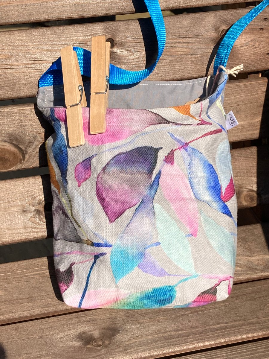 Peg bag with blue shoulder strap. Grey with colourful leaf design. Seconds