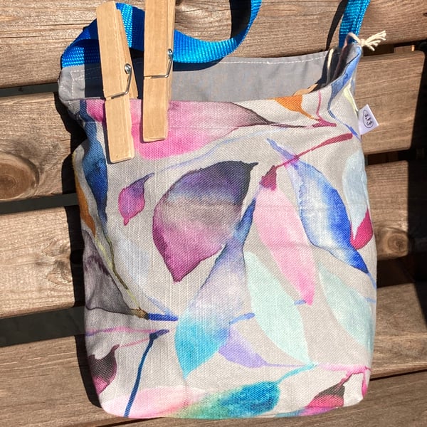 Peg bag with blue shoulder strap. Grey with colourful leaf design. 