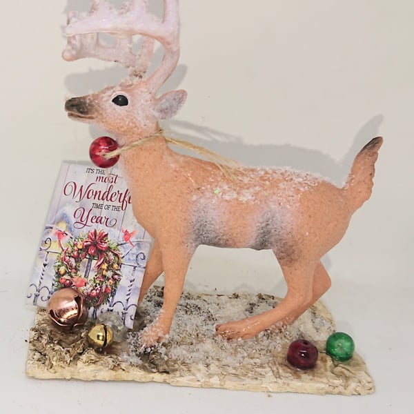 Stag on a bark slice with tiny bells and baubles in a snow scene 