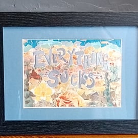Print of collage "Everything Sucks", in blue mount, framed in black.