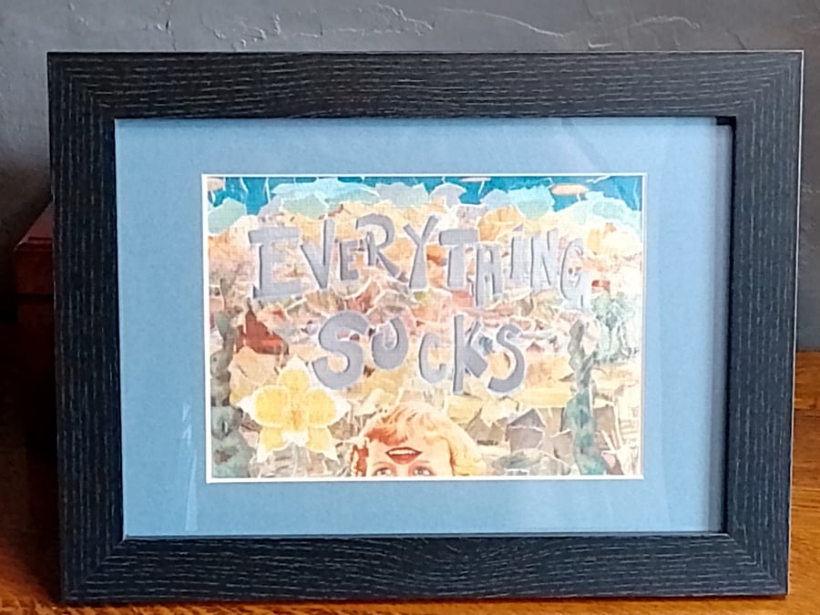 Print of collage "Everything Sucks", in blue mount, framed in black.