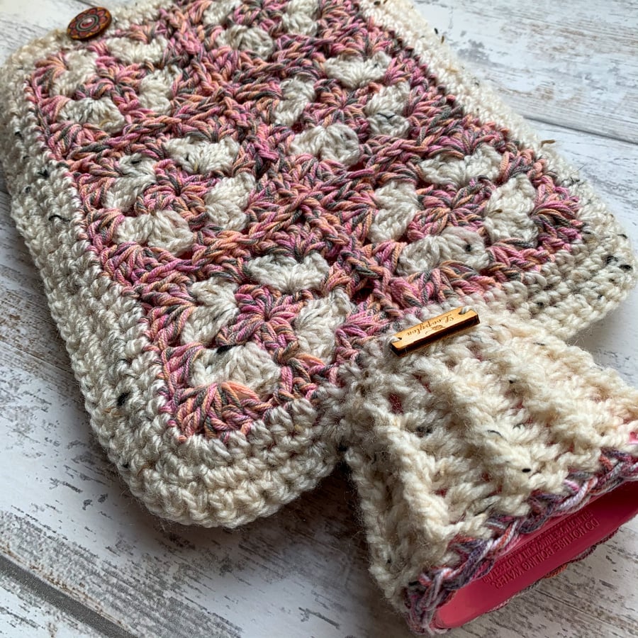 A hot water bottle and handmade crocheted cover in pink and tweed