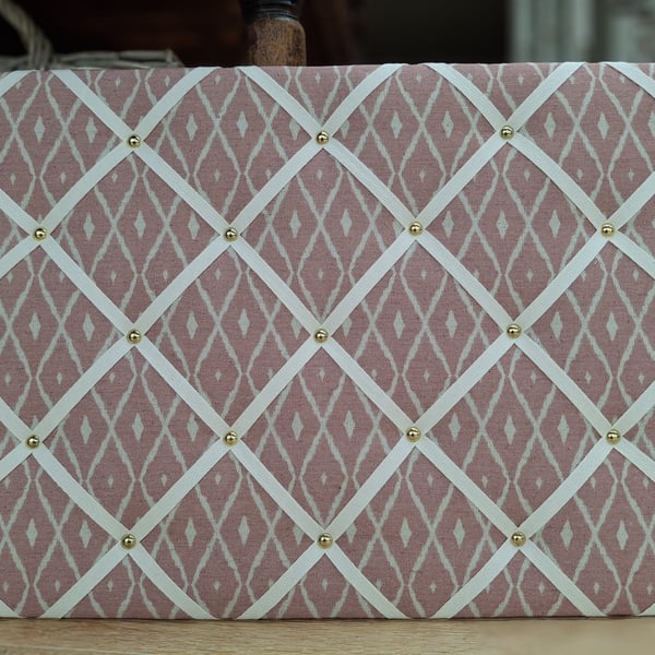 Pink noticeboard with cream cotton herringbone webbing and brass studs. 