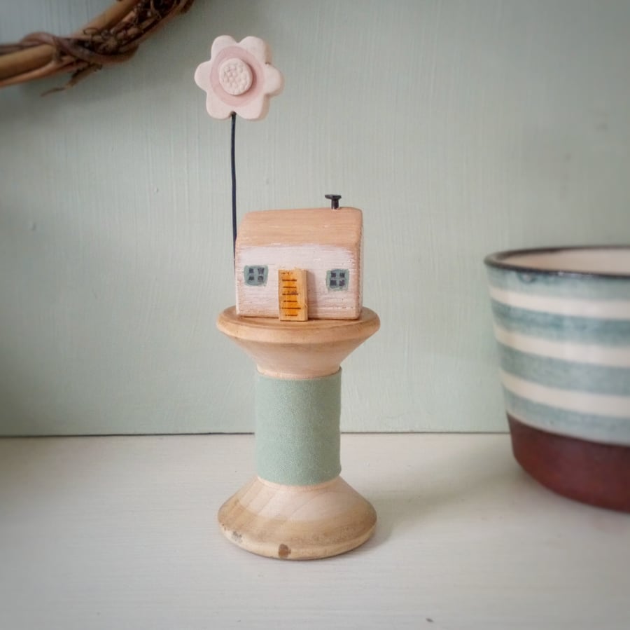 Tiny oak house with clay flower on vintage wooden bobbin