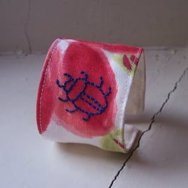 Hand embroidered textile cuff with beetle on poppy fabric