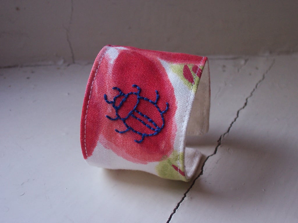 Hand embroidered textile cuff with beetle on poppy fabric