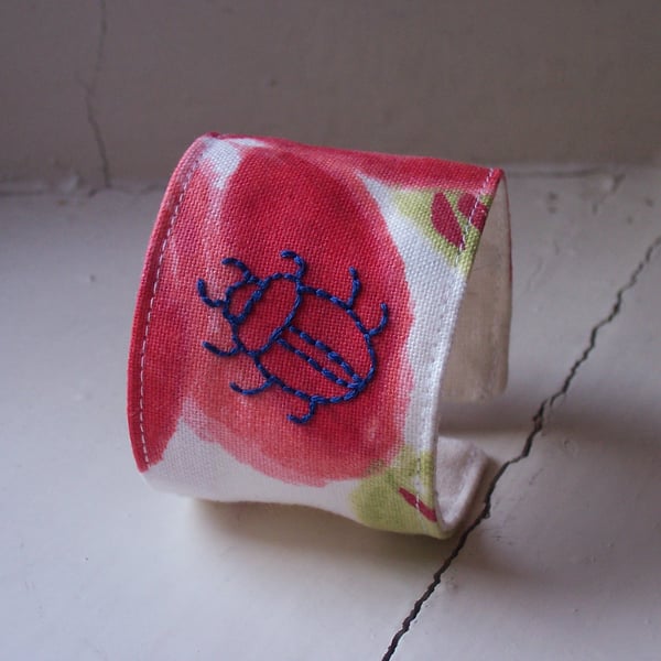 Hand embroidered textile cuff with beetle on poppy fabric