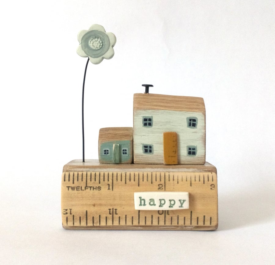 Little happy wooden houses with clay flower on a vintage ruler block