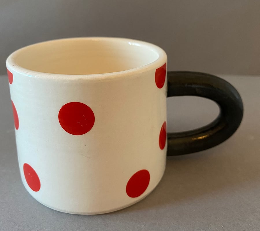 Red spotty, black handled ceramic cup.