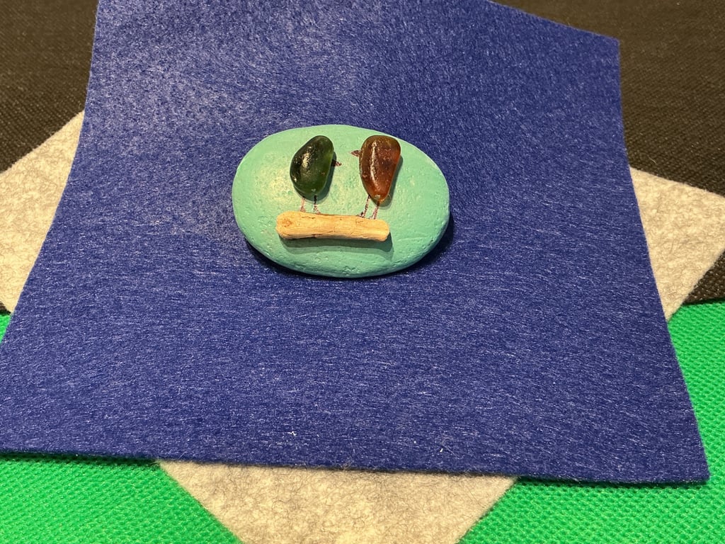 Hand painted pebble with 2 birds on a branch.