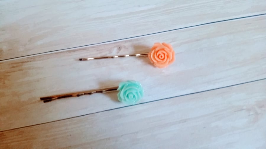 Orange and green pastel coloured  floral bobby pins on a cold coloured pin