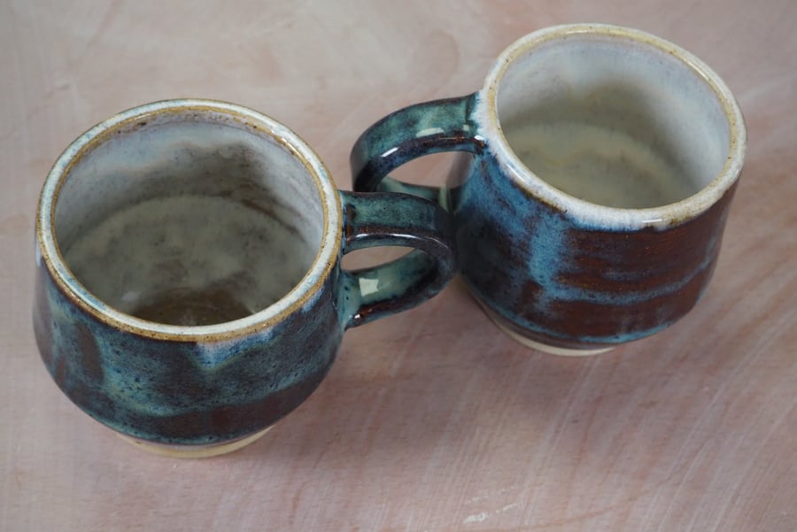 Pottery mug finished in a blue translucent glaze. Angular shape.