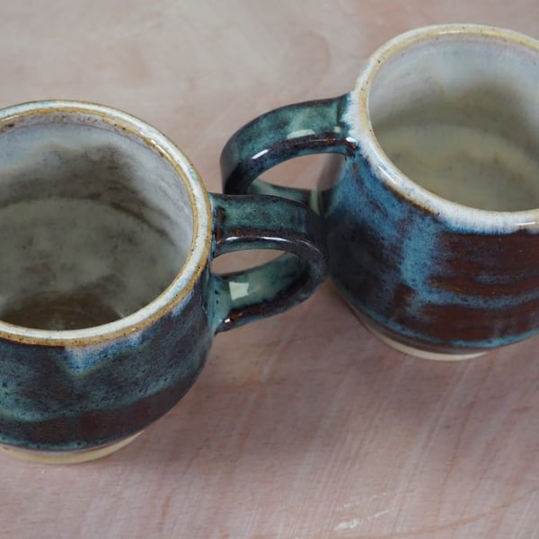 Pottery mug finished in a blue translucent glaze. Angular shape.