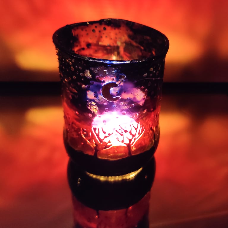 Handmade glass painted tea light candle holder with row of naked trees on sunset