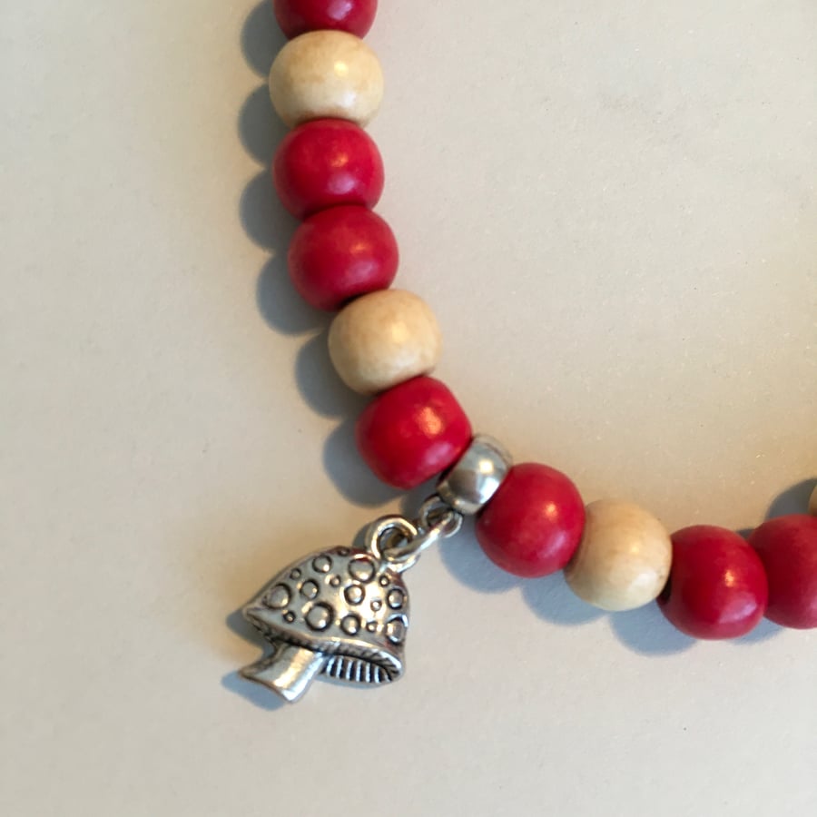 Bracelet; red and cream wooden beads, silver alloy toadstool charm