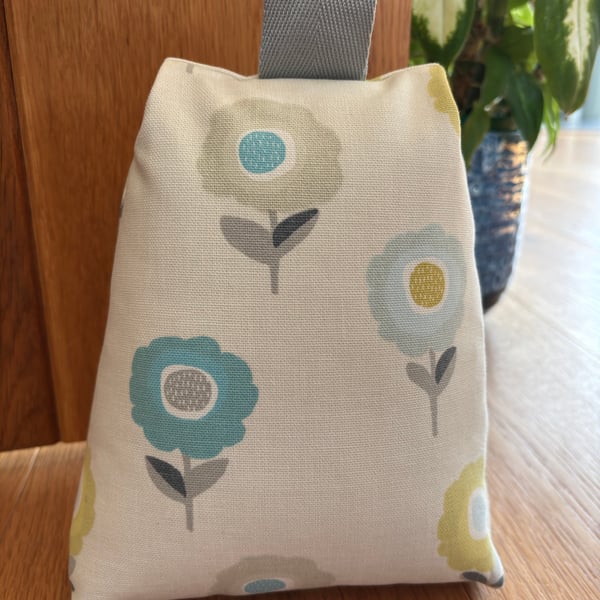 Cotton fabric doorstop in cream with bright floral pattern, filled with pebbles.