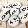 Birthday year badges black letters 'Branson' font. Sizes: 25mm, 38mm Pin