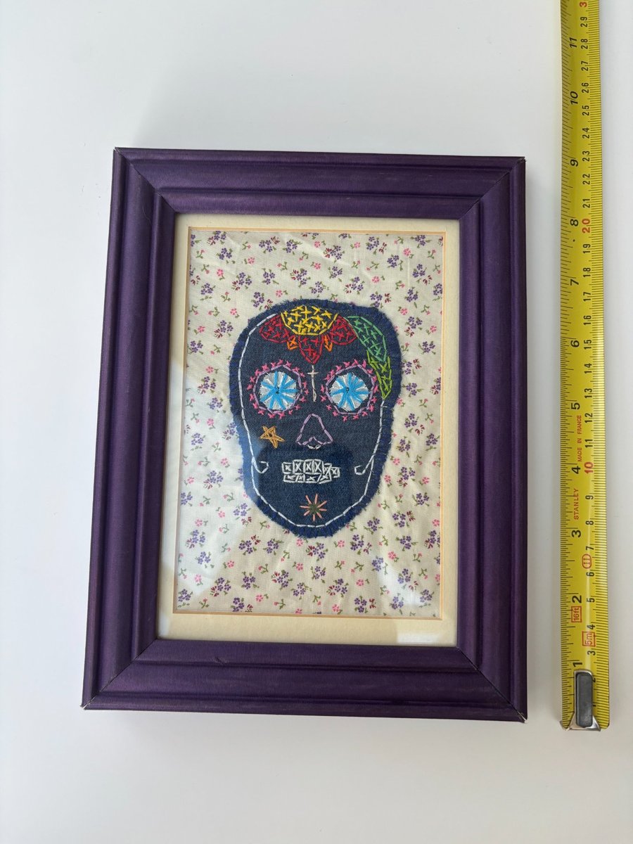 Textile art sugar skull in a purple frame.