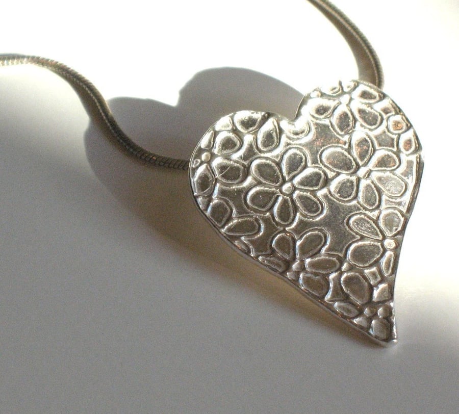 Silver heart necklace with daisy pattern.