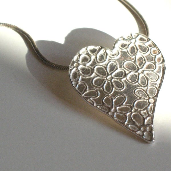 Silver heart necklace with daisy pattern.