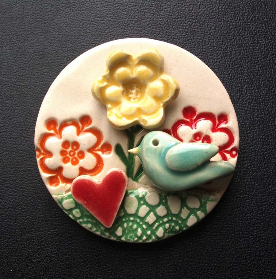 Ceramic brooch with flowers and bird.