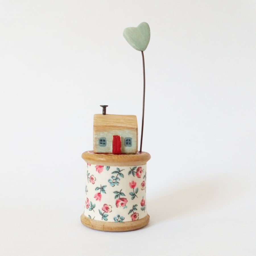 Tiny oak house with clay heart on vintage wooden bobbin