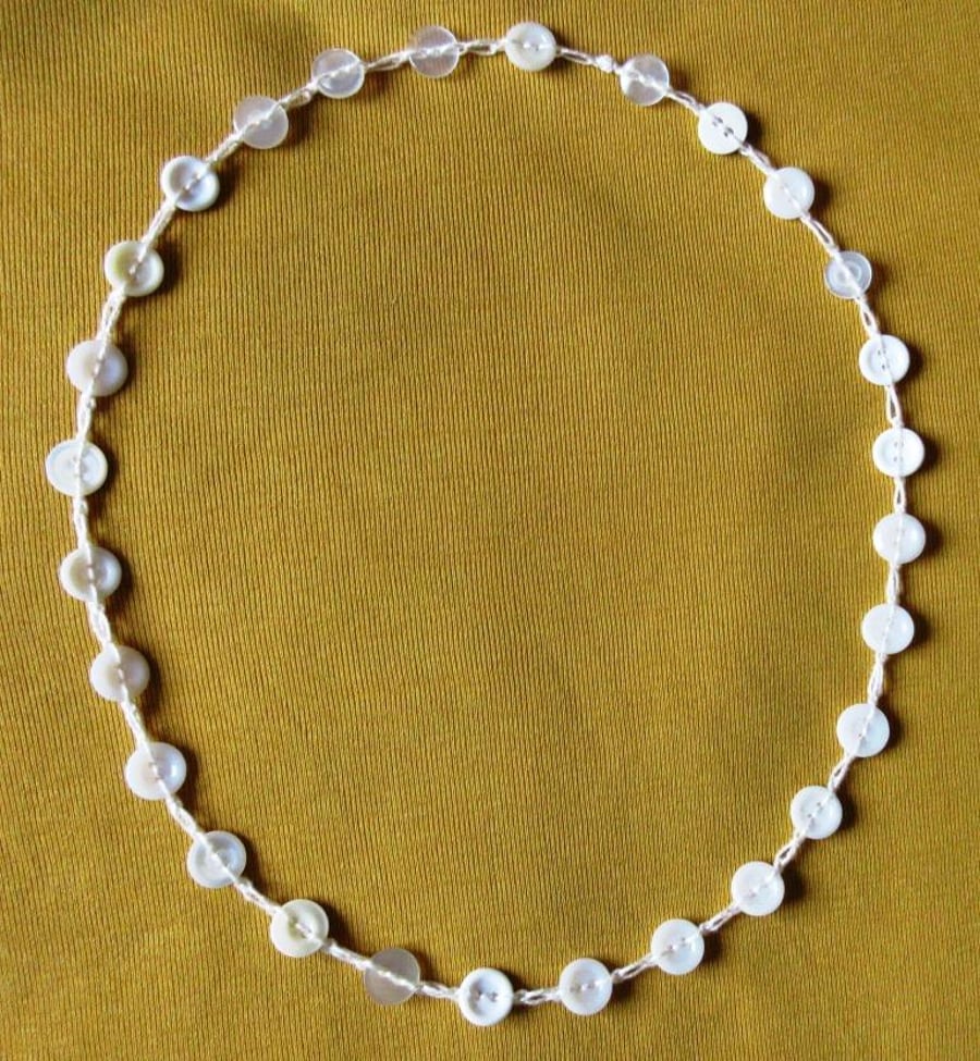 A button necklace comprising small pearly and white buttons on a crocheted chain