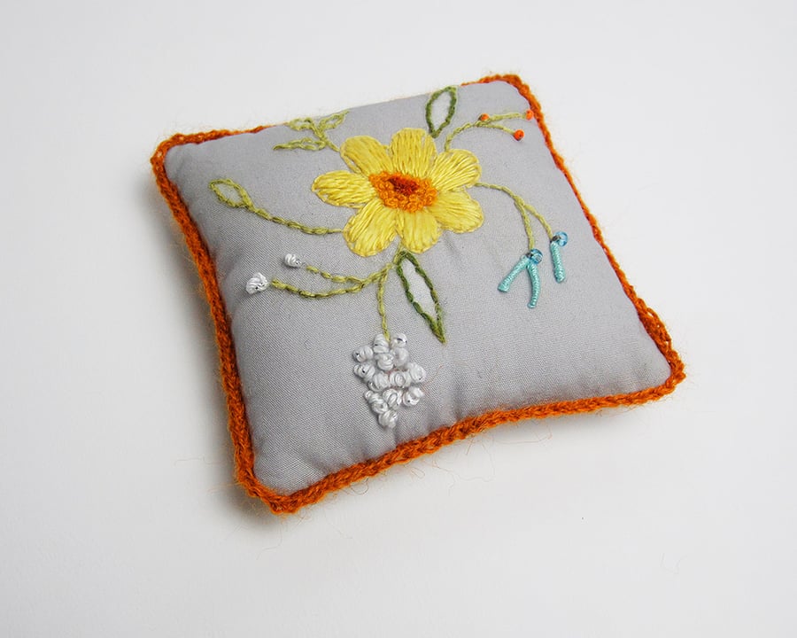 Grey pincushion with hand embroidered spring flowers and orange crochet trim