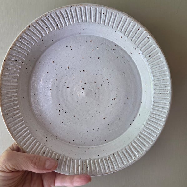 White speckled deep pottery plate with incised decorative edging 
