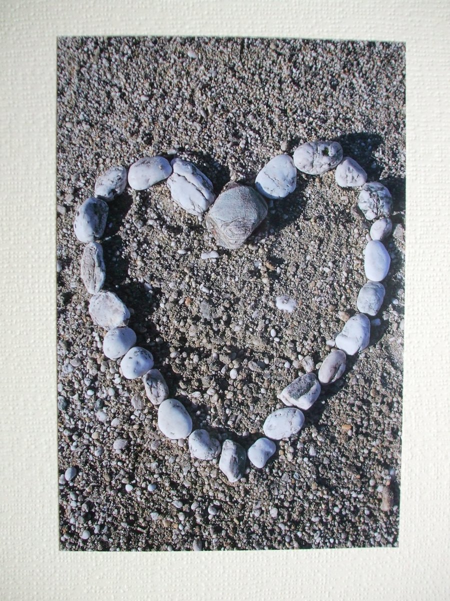  Photographic greetings card of pebbles in a heart shape on a beach.