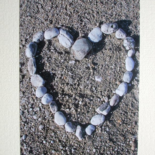  Photographic greetings card of pebbles in a heart shape on a beach.