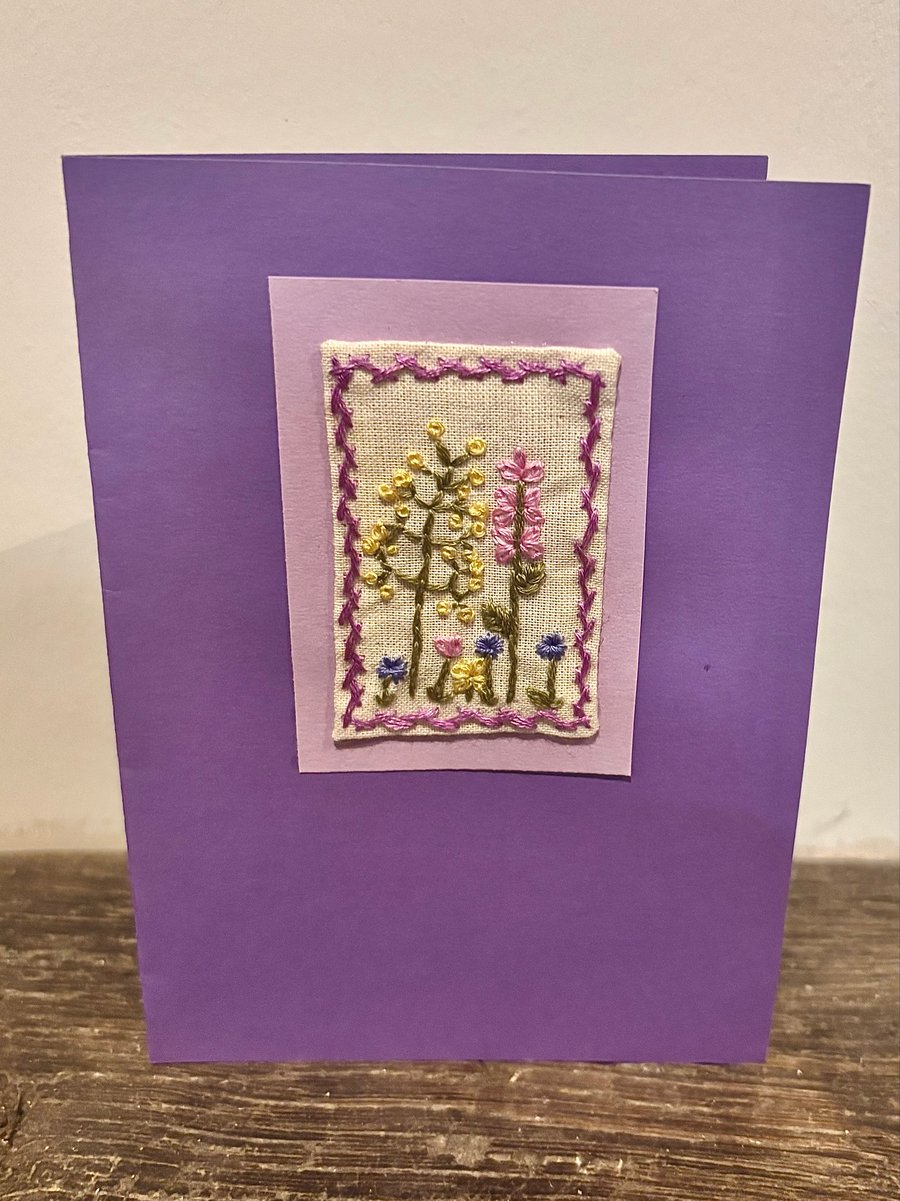 Hand embroidered purple card depicting a range of wild flowers