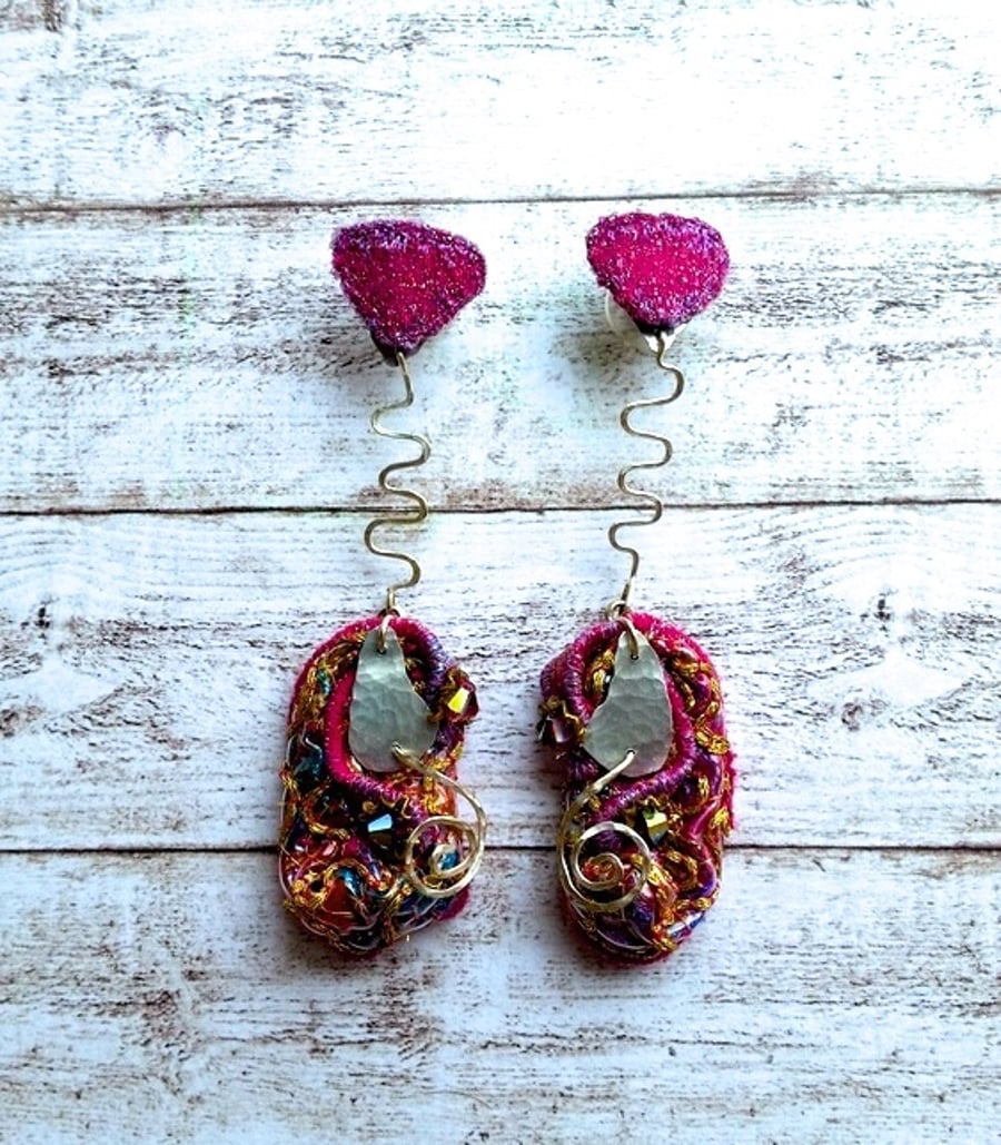 Embroidered sculptural earrings hanging from heart shape.