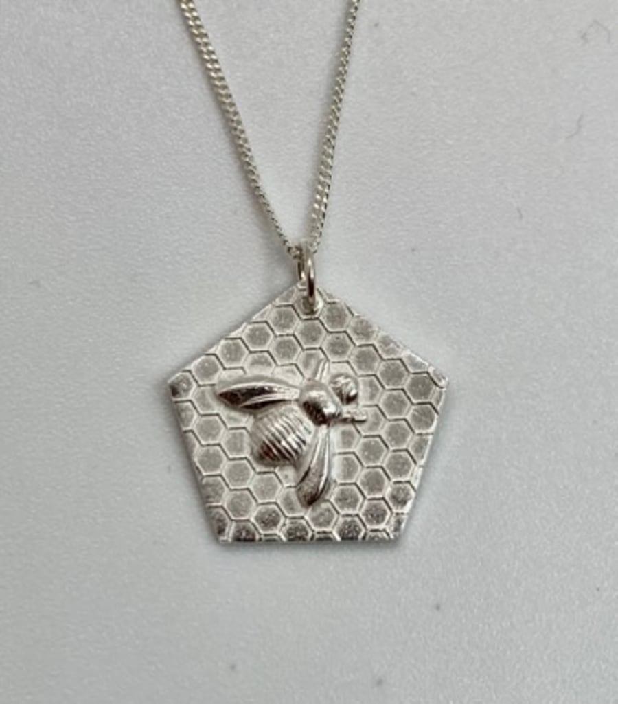 Silver bee necklace on a honeycomb background