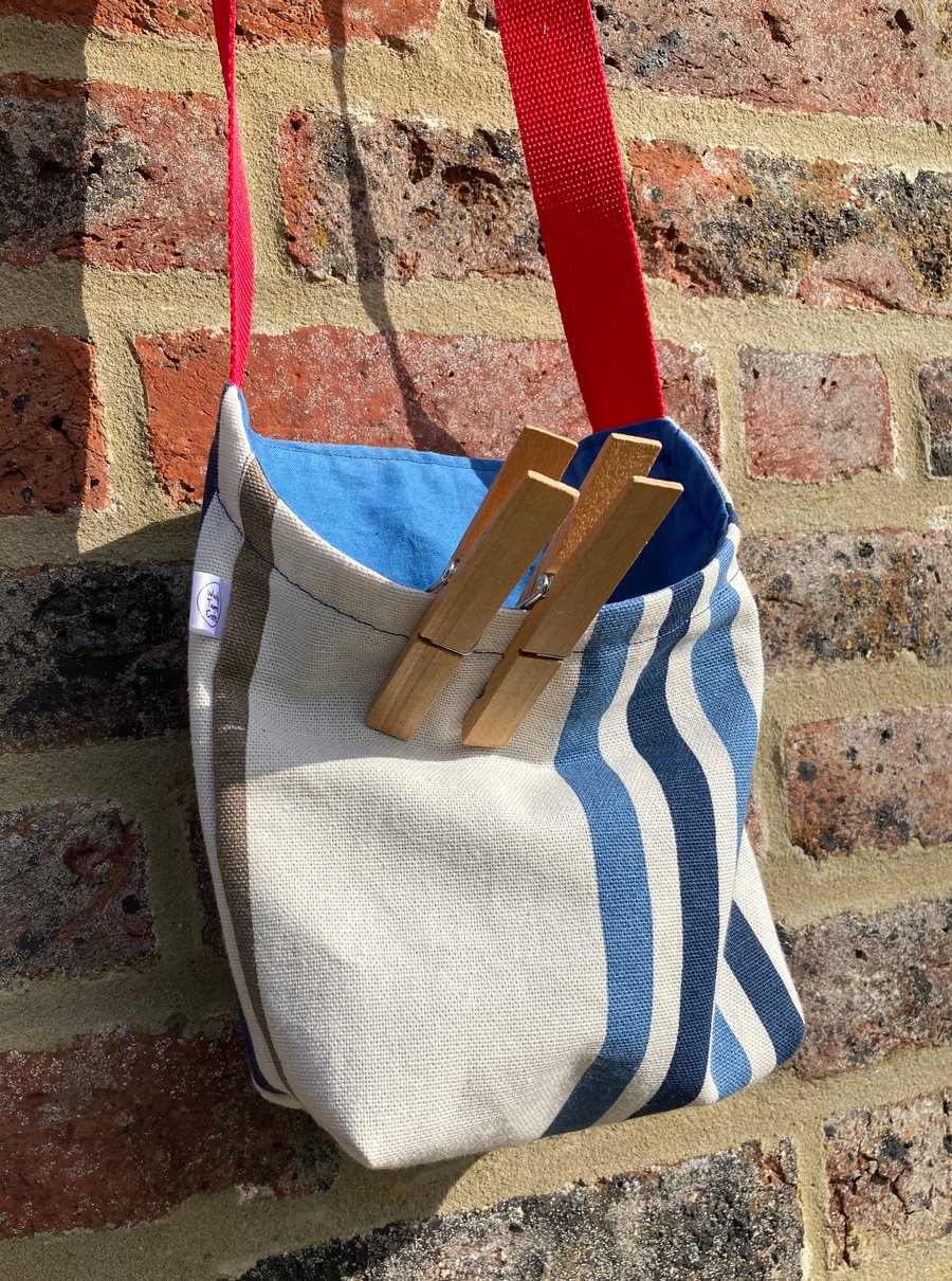Peg bag with red shoulder strap. Stripes in blue and cream
