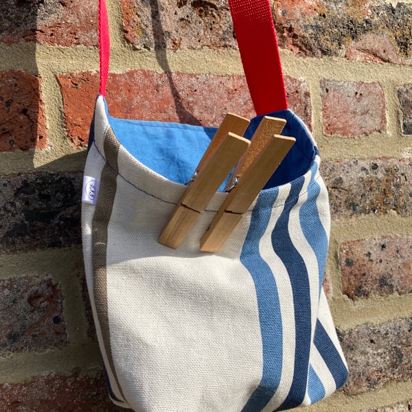 Peg bag with red shoulder strap. Stripes in blue and cream