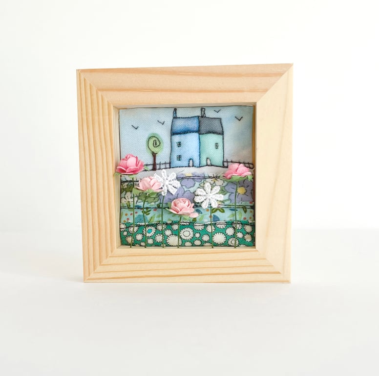 Fabric picture of houses and flowers, in a small wooden frame