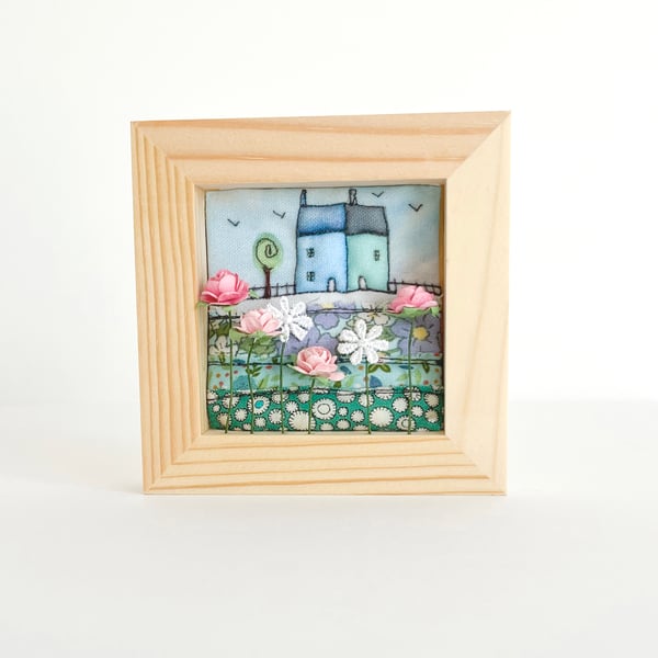 Fabric picture of houses and flowers, in a small wooden frame