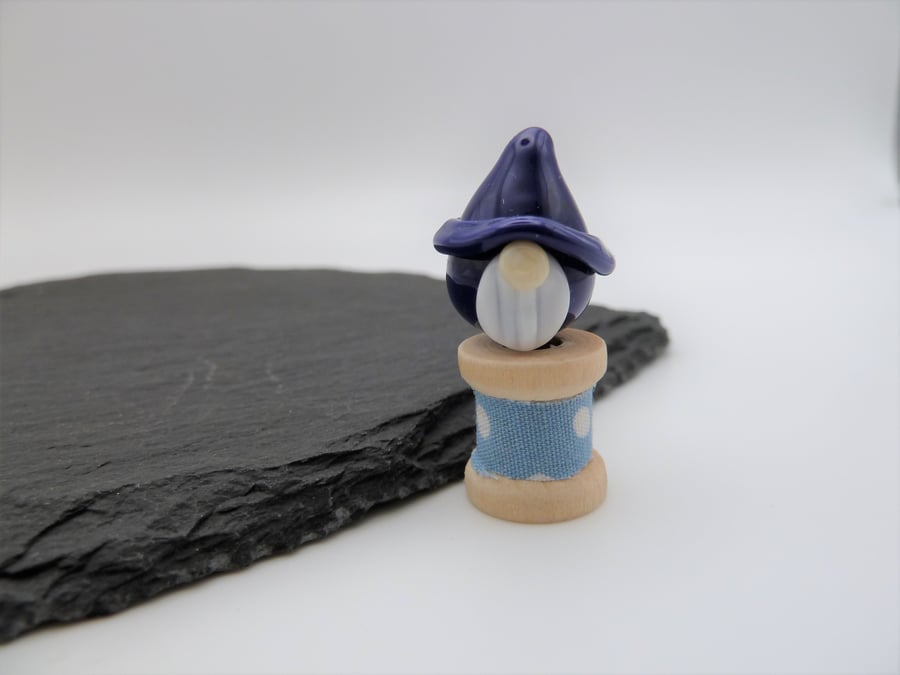 small glass gnome on a wooden bobbin
