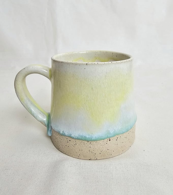 A handmade stoneware mug in yellow, green and oatmeal