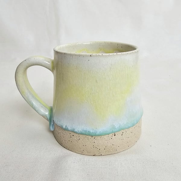 A handmade stoneware mug in yellow, green and oatmeal