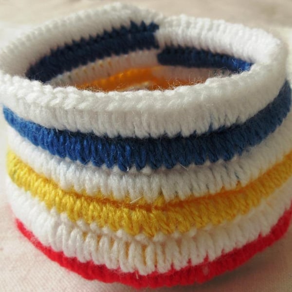 A small crochet basket or bowl in white acrylic yarn with multi-coloured stripes