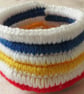 A small crochet basket of bowl in white acrylic yarn with multi-coloured stripes