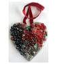 A wooden heart shaped pendant with ruby and black coloured spheres.