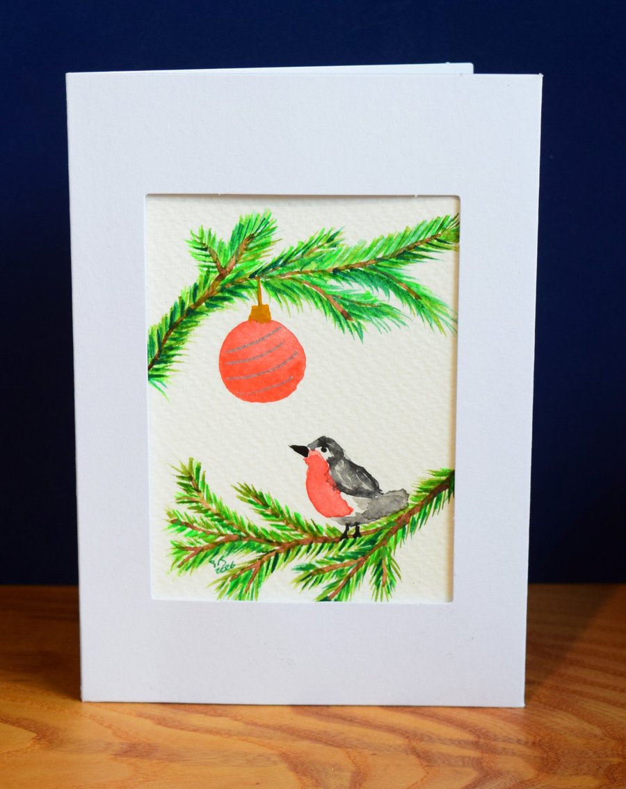 Festive robin on evergreen branches, with red bauble