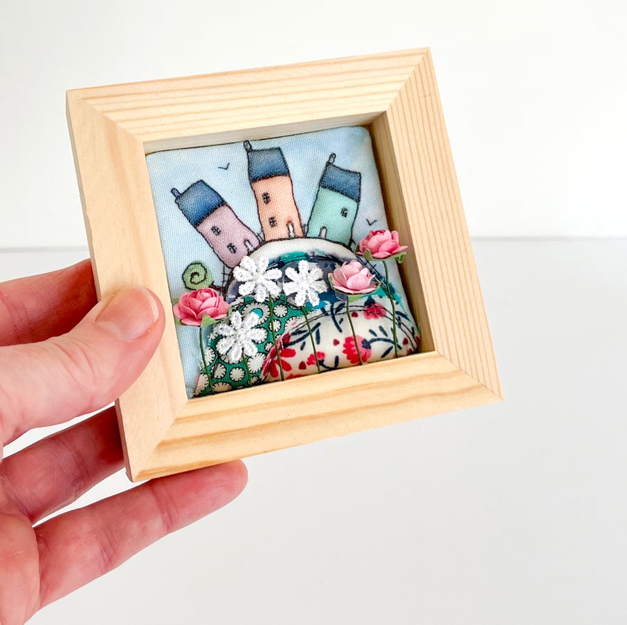 Little houses on a fabric hill, with flowers, in small wooden frame