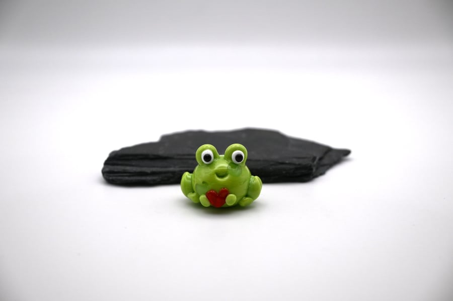 small glass frog holding a heart figure
