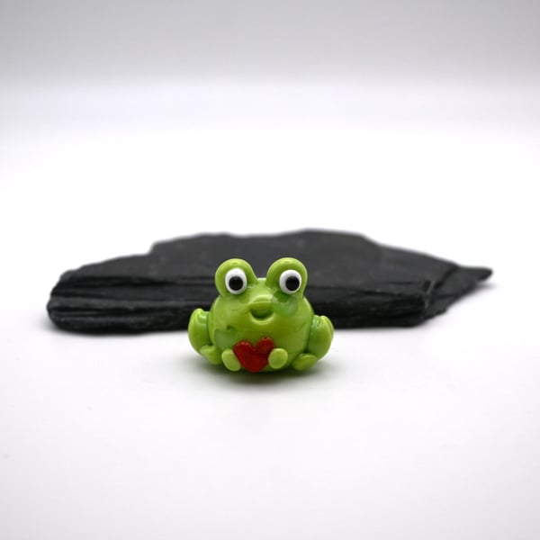 small glass frog holding a heart figure