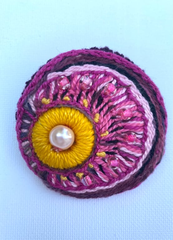 Hand embroidered circular brooch in shades of pink with added beads